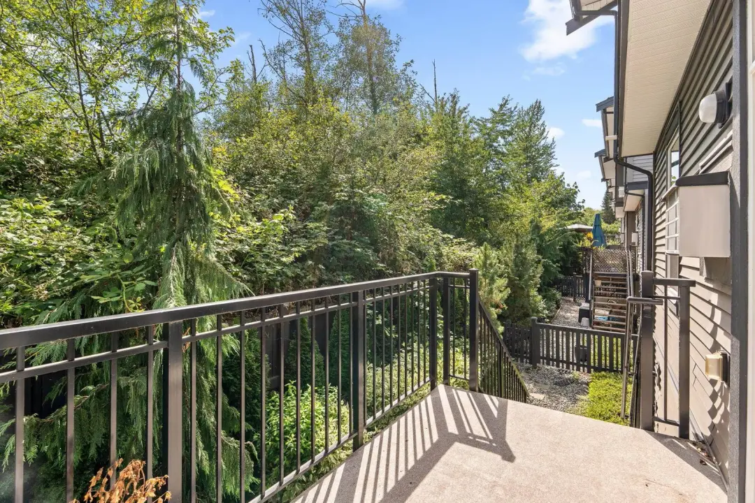 Frame balcony with black railing, exterior sconces, and stairs to yard