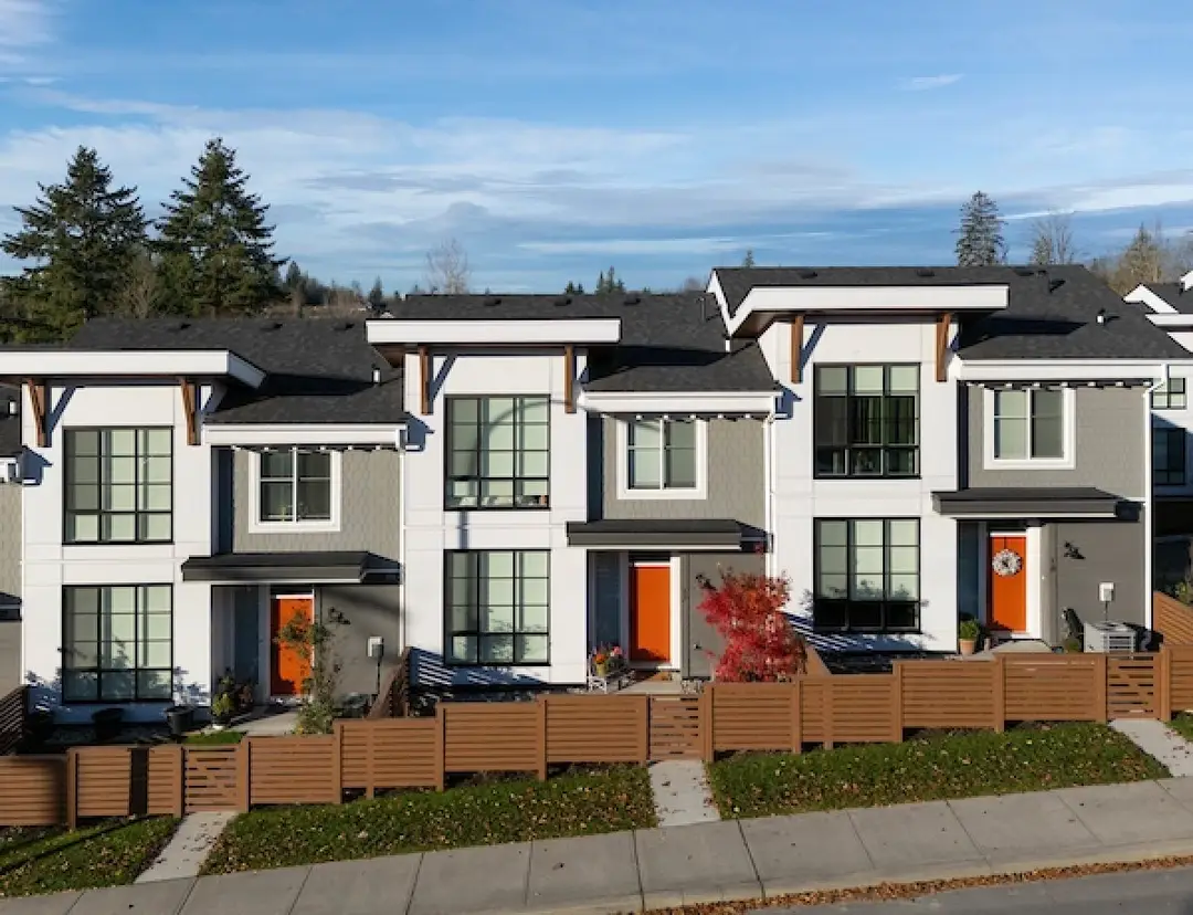 Daylight facade of white Windfall townhomes with wood garage doors in Maple Ridge
